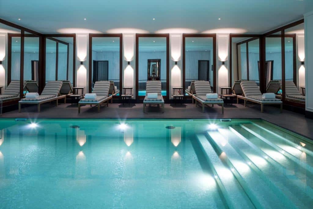 Piscina interior do J.K. Place Paris, rodeada de espreguiçadeiras, toalhas e grandes espelhos na parede.