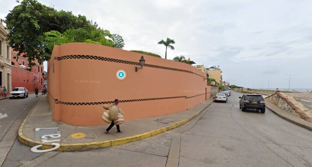 Rua de Cartagena ladeada por um muro alto cor de salmão com padrão xadrez a preto e branco, com o mar visível ao fundo.