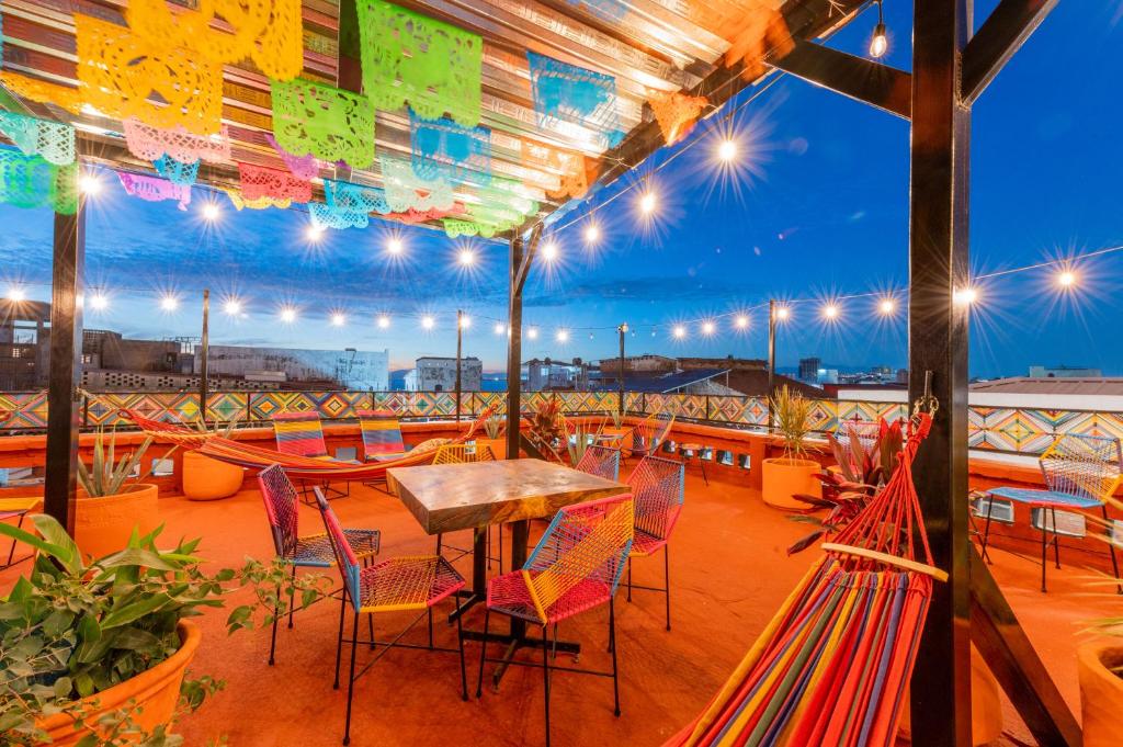 Um pátio na cobertura da Casa Colibrí Malecón com cadeiras coloridas, redes, fios de luzes, bandeirolas de papel picado e vistas da cidade ao anoitecer.