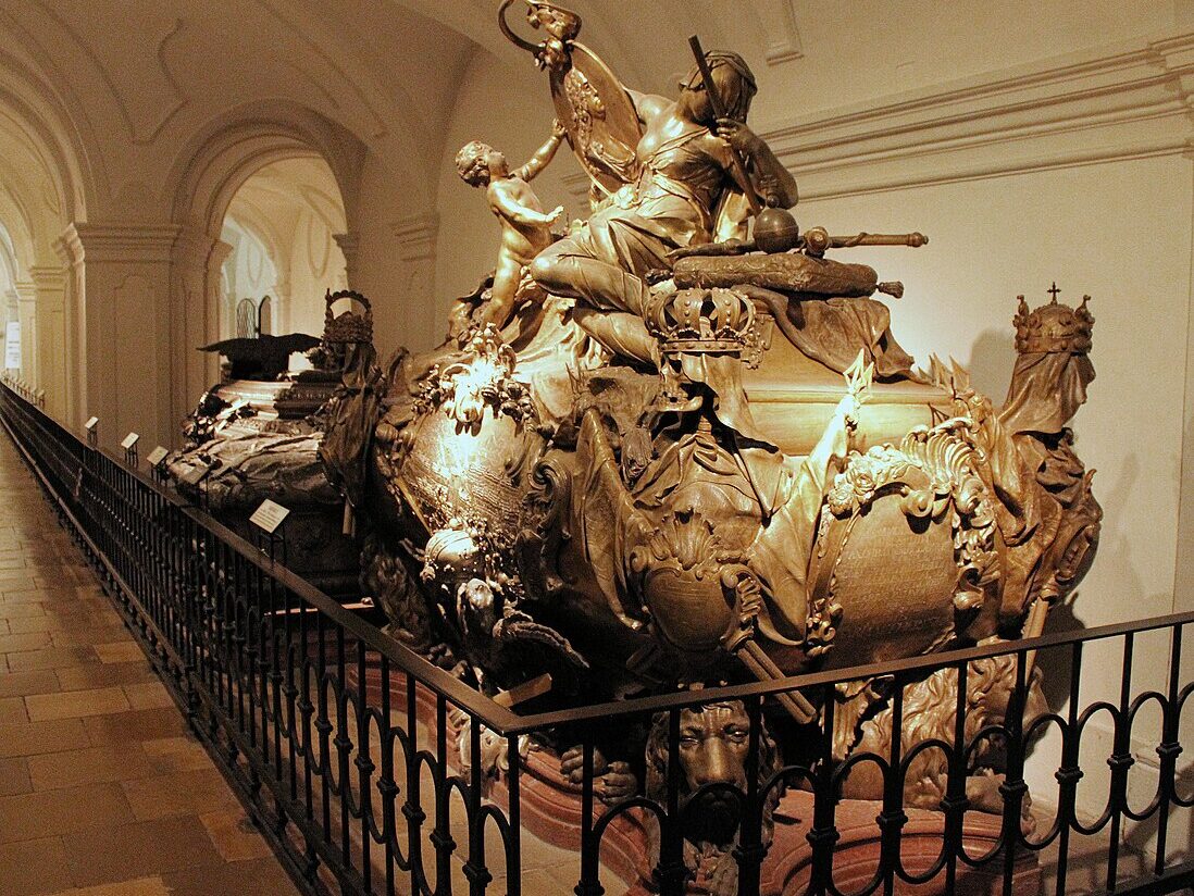 Sarcófago da Cripta Imperial, com esculturas detalhadas e coroas, exposto num corredor com pouca luz.