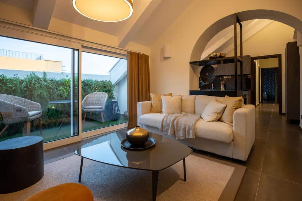 Sala de estar acolhedora do Margherita Apartments com sofá bege, mesa de centro de vidro e estante de madeira escura, iluminada por candeeiros suspensos.