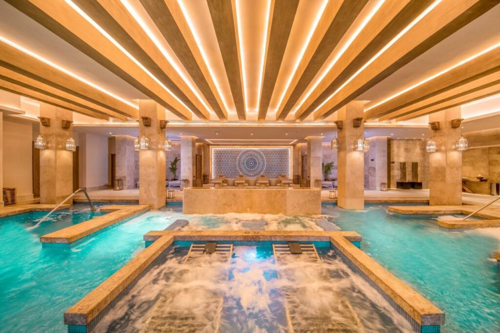 Piscina coberta no Haven Riviera Cancun Adults Only, espaço amplo em tons dourados com espreguiçadeiras submersas