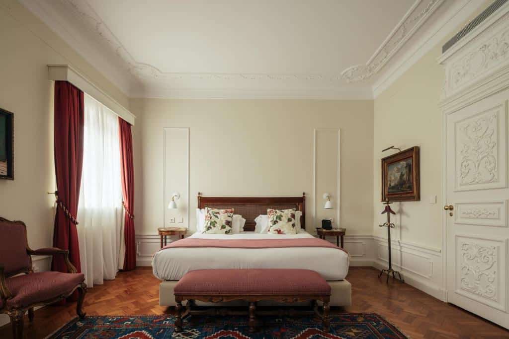 Quarto amplo do Hospes Infante Sagres Porto, com cama ao centro, duas mesinhas de cabeceira e uma poltrona.