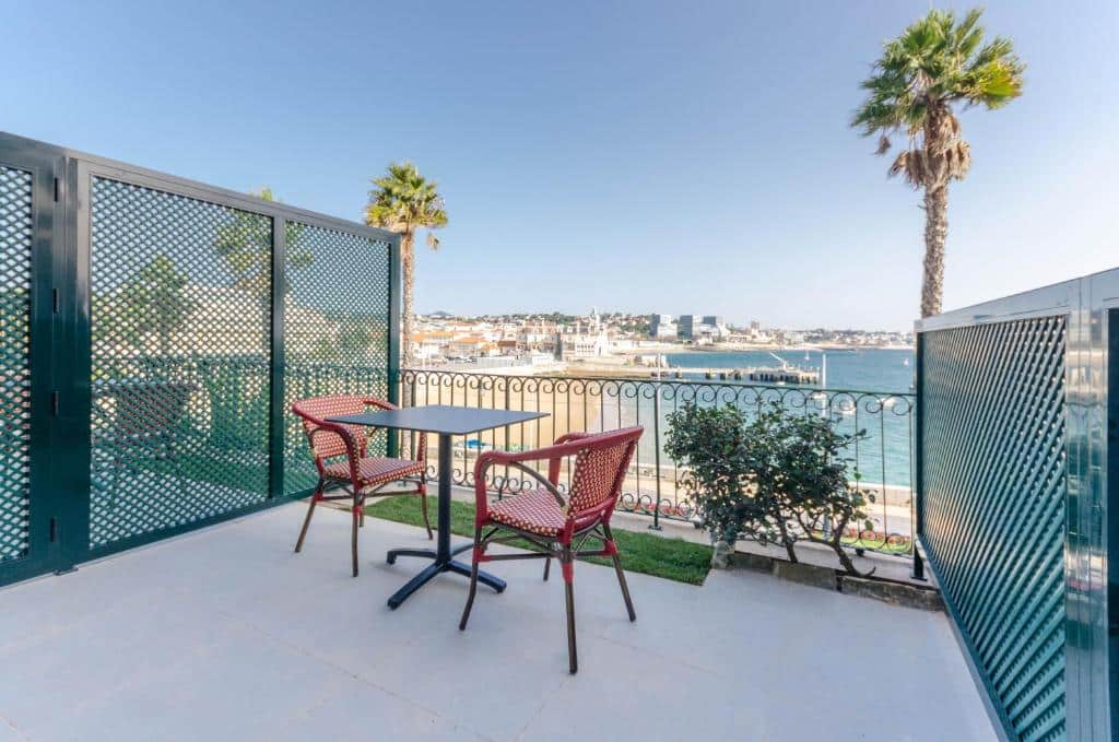 Varanda do Westlight Cascais Chalet com vista direta para o mar, uma mesa quadrada e duas cadeiras vermelhas