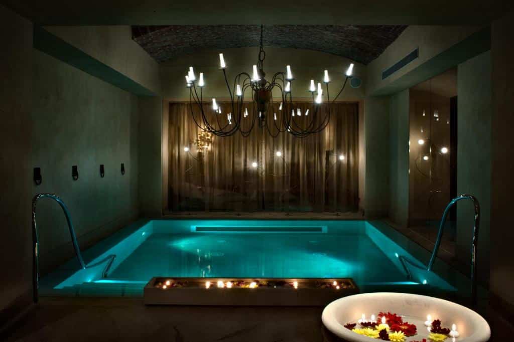 Piscina interior do Château Monfort – Relais &amp; Châteaux com um lustre no teto, num ambiente mais escuro e intimista