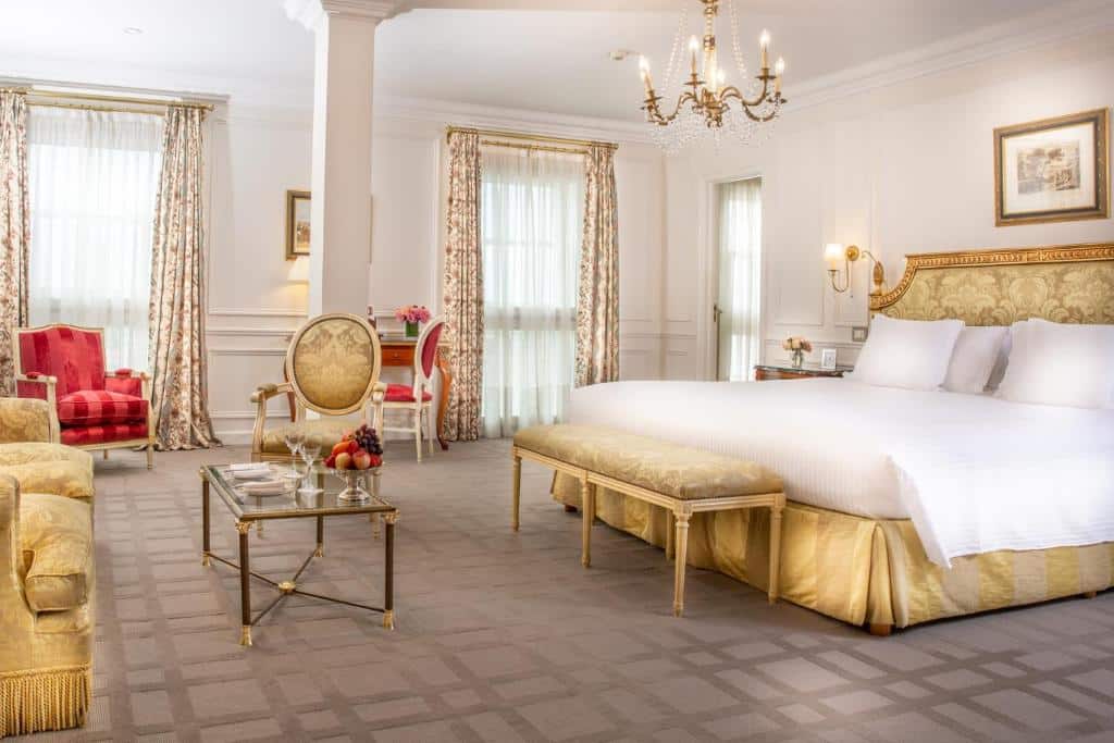 quarto amplo do Alvear Art Hotel com decoração clássica com detalhes dourados e vermelhos, cama de casal, poltronas, candeeiro de teto e janelas grandes com cortinas
