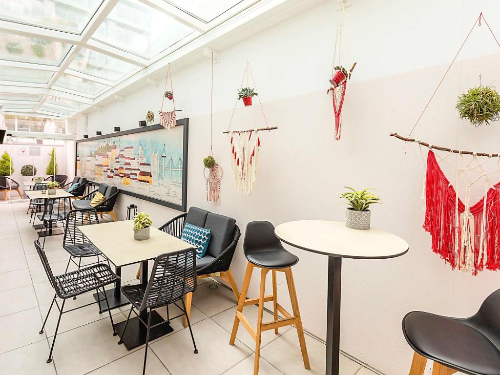 Área de convívio e refeições do Ibis Lisboa Parque das Nações com mesas de madeira, pequenos sofás e cadeiras, decoração com pequenos vasos de flores e um quadro com uma imagem de Lisboa