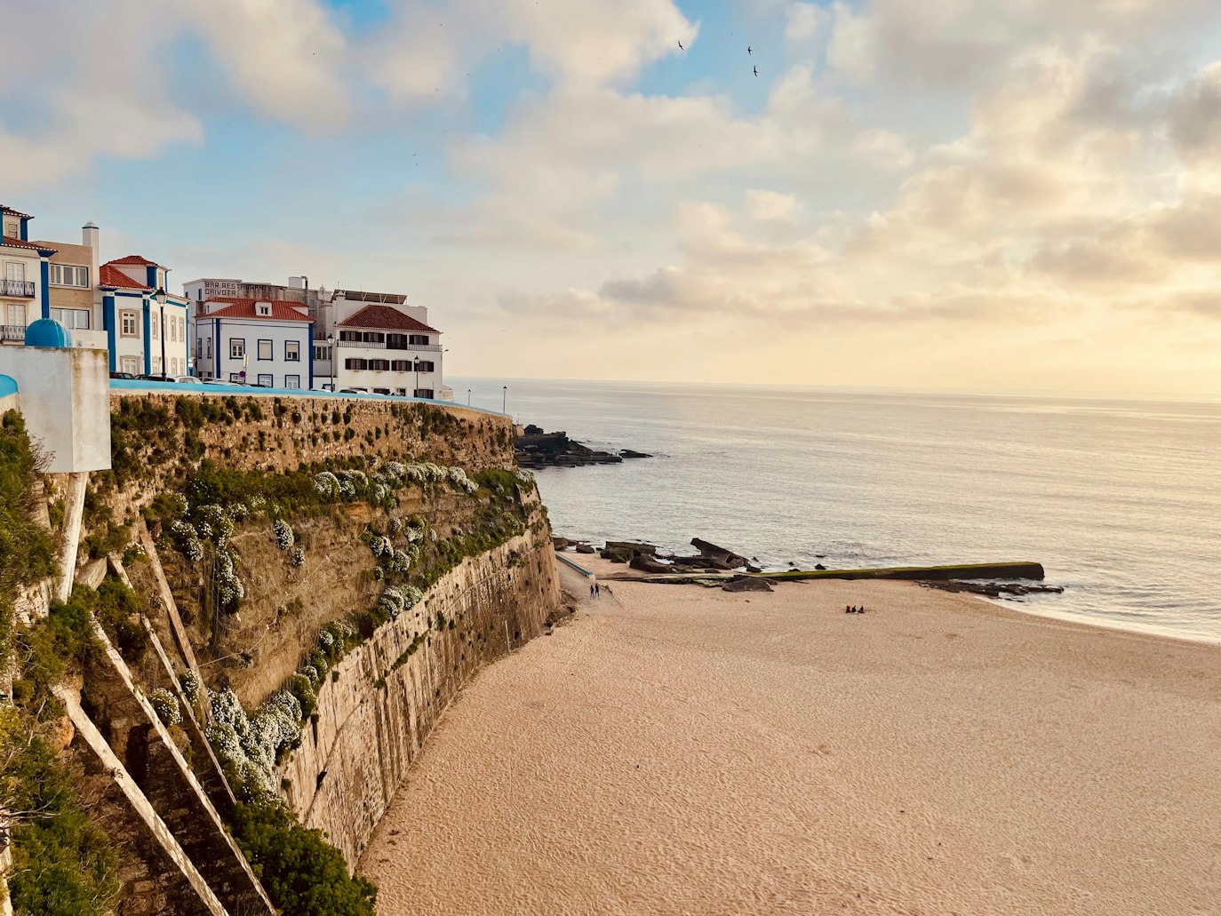 Cena costeira na Ericeira, com casas no topo de uma falésia rochosa e vista para uma praia de areia.