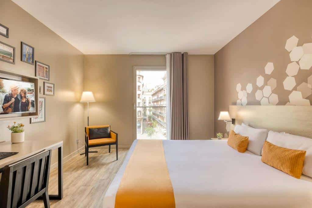 Quarto do Citadines Ramblas Barcelona, com cama de casal, secretária com cadeira, televisão na parede e uma poltrona junto à janela com cortinas bege.