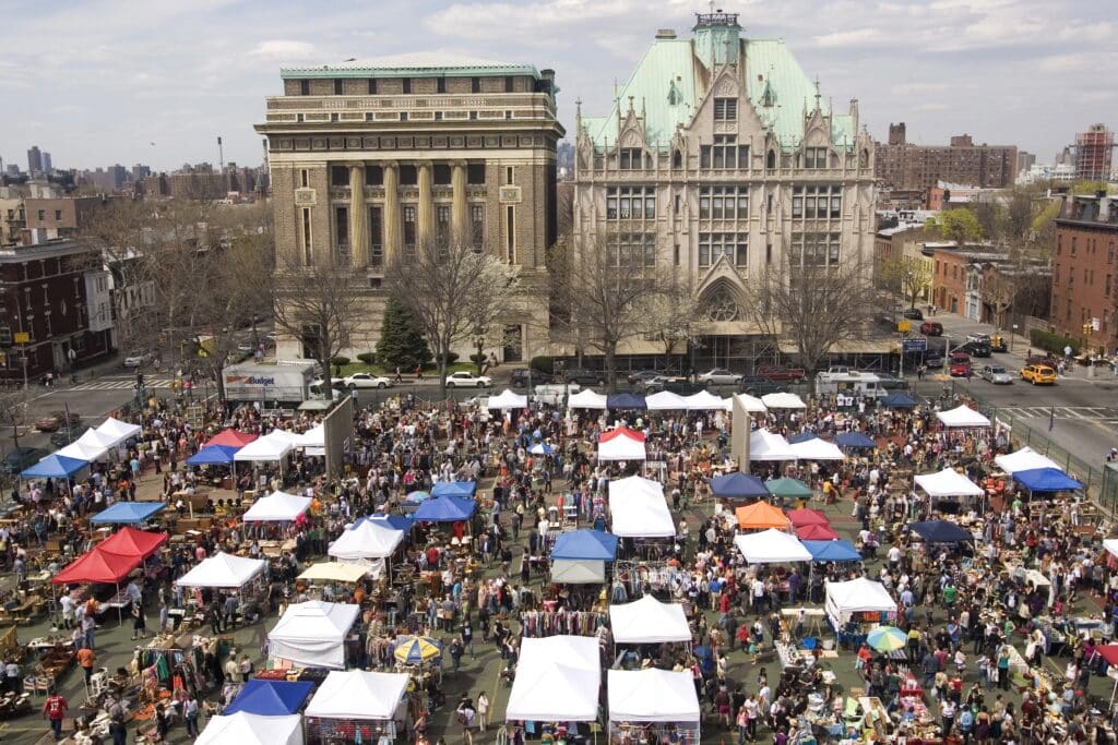 Vista aérea do Brooklyn Flea Market, com várias tendas dispostas em filas e vendedores a oferecer diversos artigos a uma multidão.