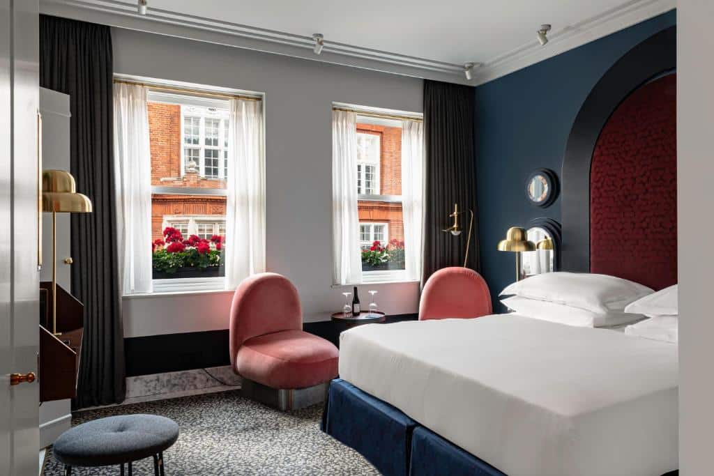 Quarto do The Henrietta Hotel com cama de casal, duas janelas com cortinas, duas poltronas e cabeceira arredondada em tons de preto e vinho
