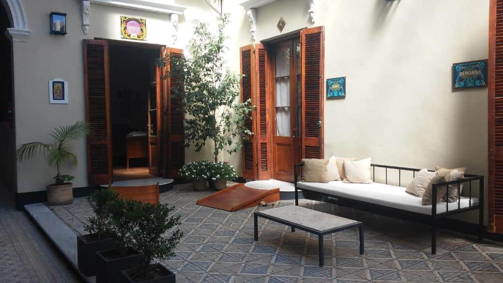 área exterior do Cruce´s Hotel Boutique, um dos hotéis no centro de Buenos Aires, com portas altas de madeira, plantas e uma árvore, um sofá baixo com almofadas e uma mesa de centro