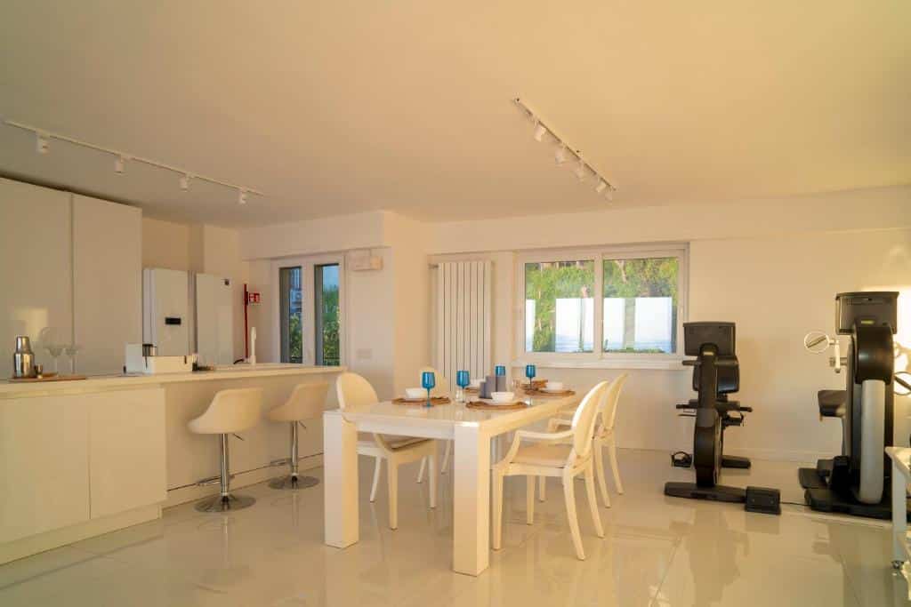 Espaçoso ambiente com mesa de jantar de madeira clara, cadeiras brancas estofadas e equipamentos como computador e máquina de café, no Caravaggio Luxury Apartment.