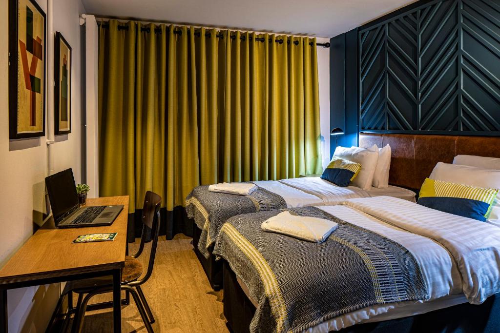Quarto do Latroupe Jacobs Inn com cortinas amarelas, parede azul-petróleo e cama de casal com roupa de cama e cobertores.