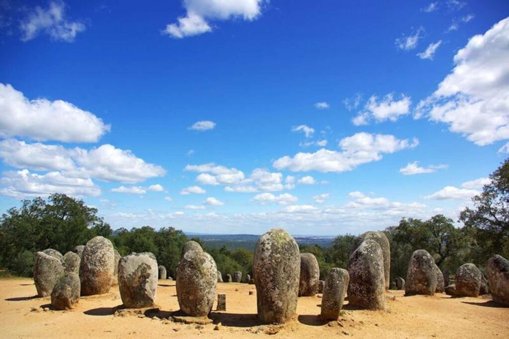 Círculo de pedras em paisagem rural com céu azul e vegetação, monumento megalítico em Portugal