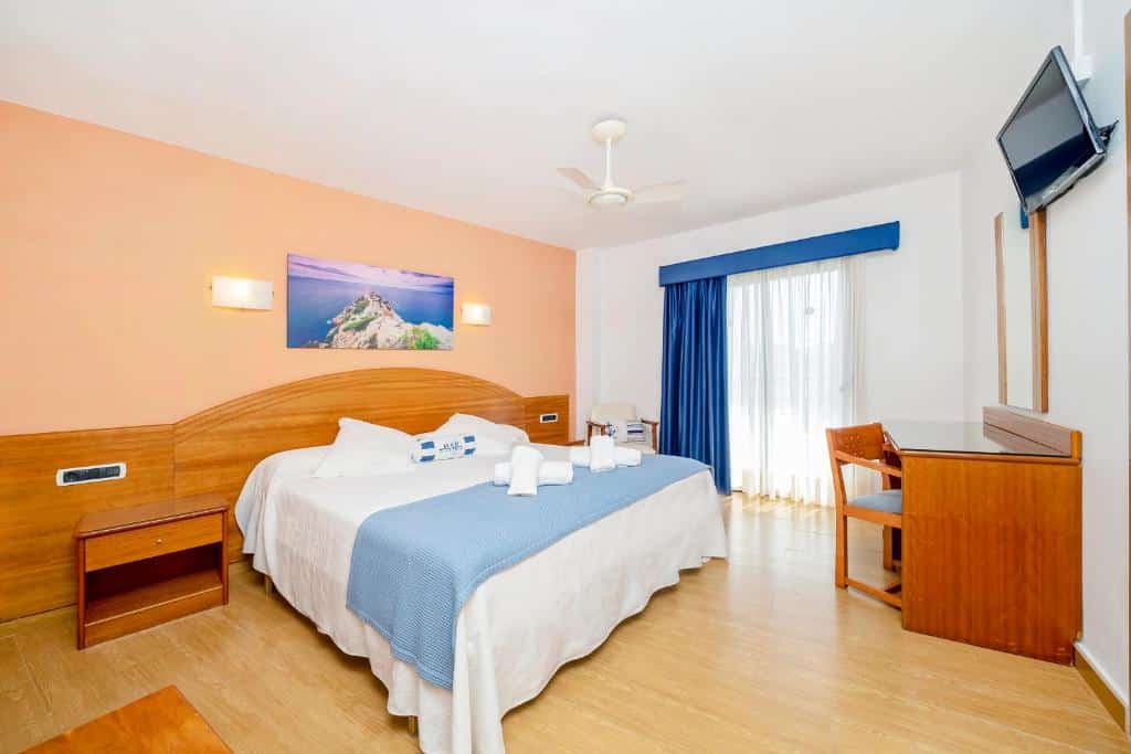 Quarto bem iluminado do Hostal Manolita com uma cama grande, secretária, TV na parede e janela com cortinas.