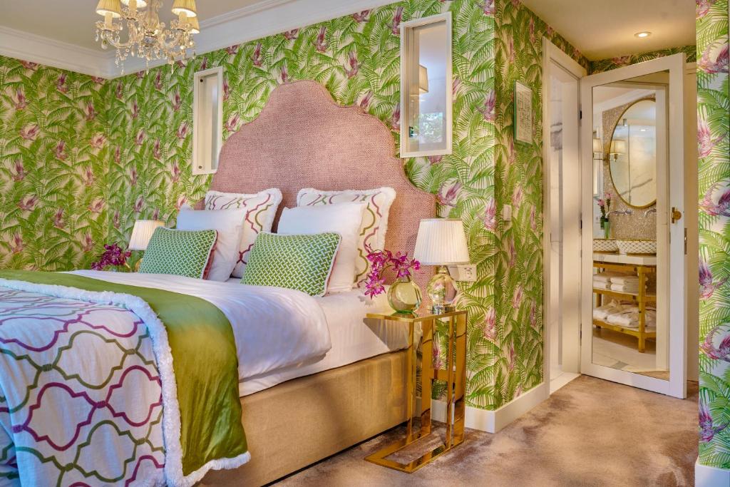 Quarto do Hotel Estheréa, que ilustra onde ficar em Amesterdão: papel de parede floral verde, uma cama grande, duas mesas de cabeceira com candeeiros e uma porta aberta para a casa de banho.