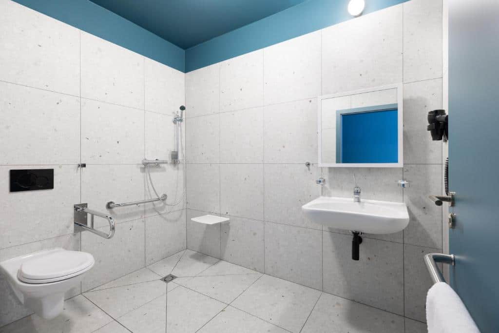 Casa de banho acessível do Hotel Beránek, com sanita suspensa, assento de duche, barras de apoio, lavatório e espelho.