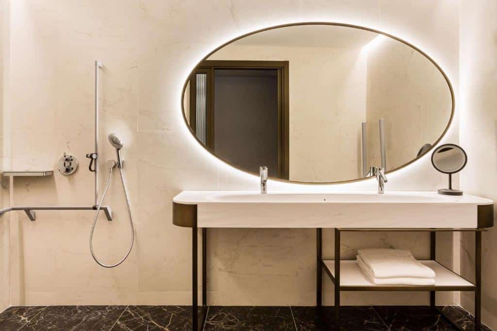 Casa de banho adaptada do Radisson Collection Hotel, Magdalena Plaza Sevilla, com barras de apoio, chuveiro de mão e lavatório rebaixado.