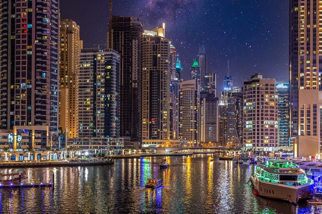 A zona da Dubai Marina à noite, com arranha-céus e barcos iluminados ao longo da marginal.