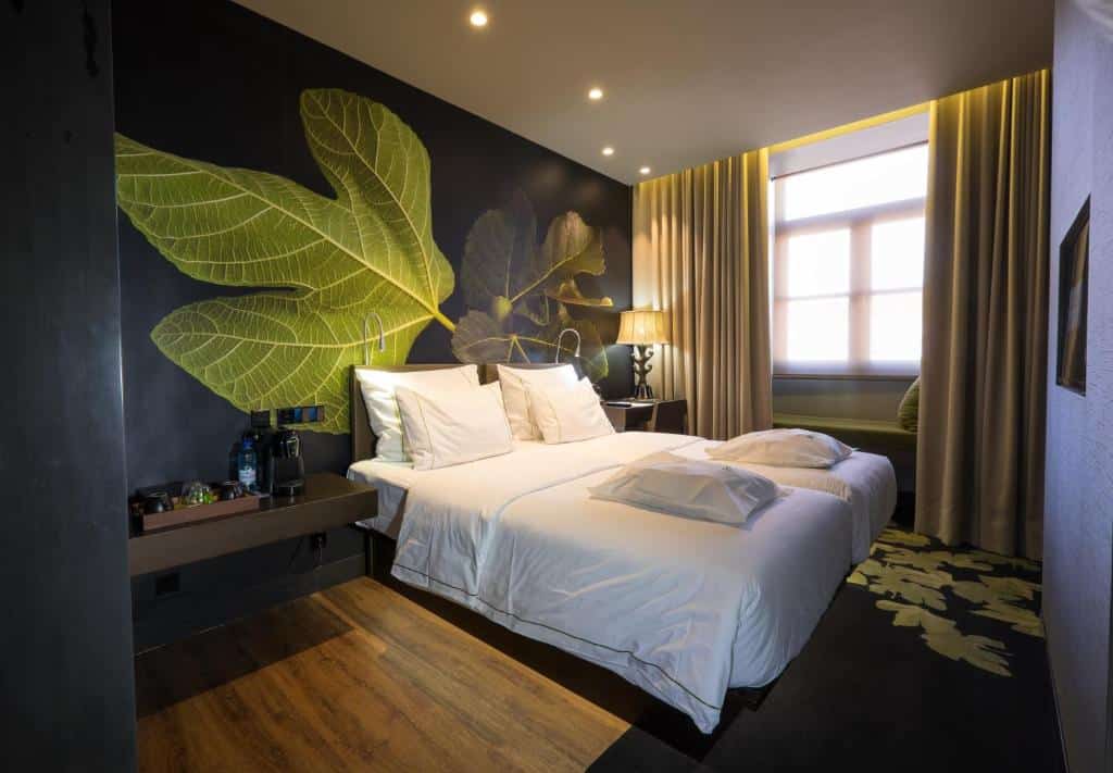 Quarto do Figueira by The Beautique Hotels com uma cama de casal, janela com cortinas, uma bancada com itens de pequeno-almoço de um lado e uma pequena mesa com cadeira do outro.