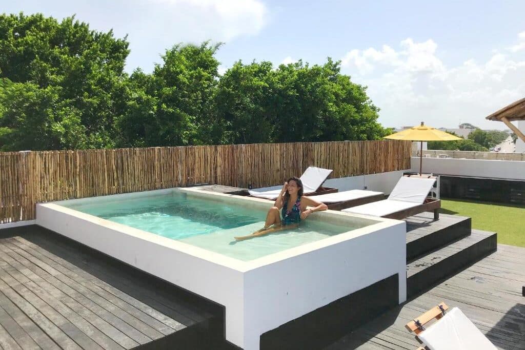 Mulher a sorrir numa piscina retangular de bordo branco, numa área de lazer com espreguiçadeiras, no Che Suites Playa.
