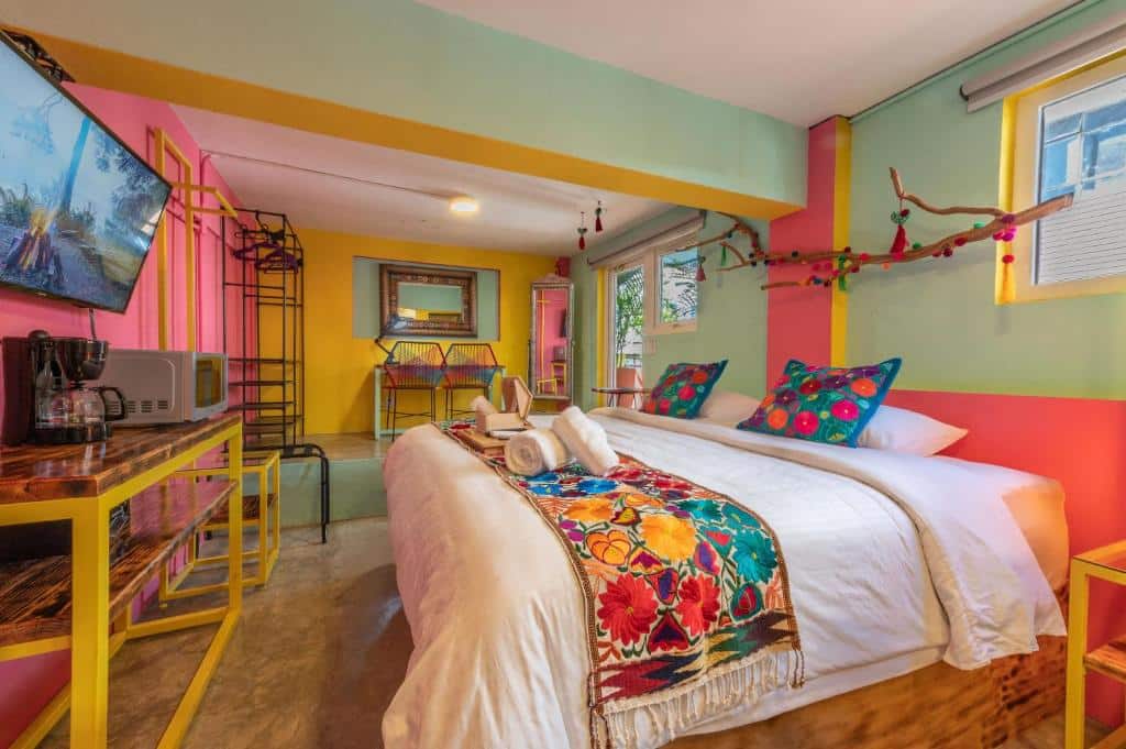 Quarto da Casa Colibrí Malecón colorido com uma cama de casal, paredes claras, uma TV na parede e um ramo decorativo por cima da cama.