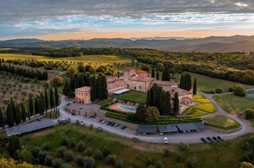 Vista aérea do hotel de cinco estrelas Borgo Scopeto, com muita vegetação em redor, céu ao fim da tarde num tom laranja e azul, e edifícios com aspeto de castelo medieval