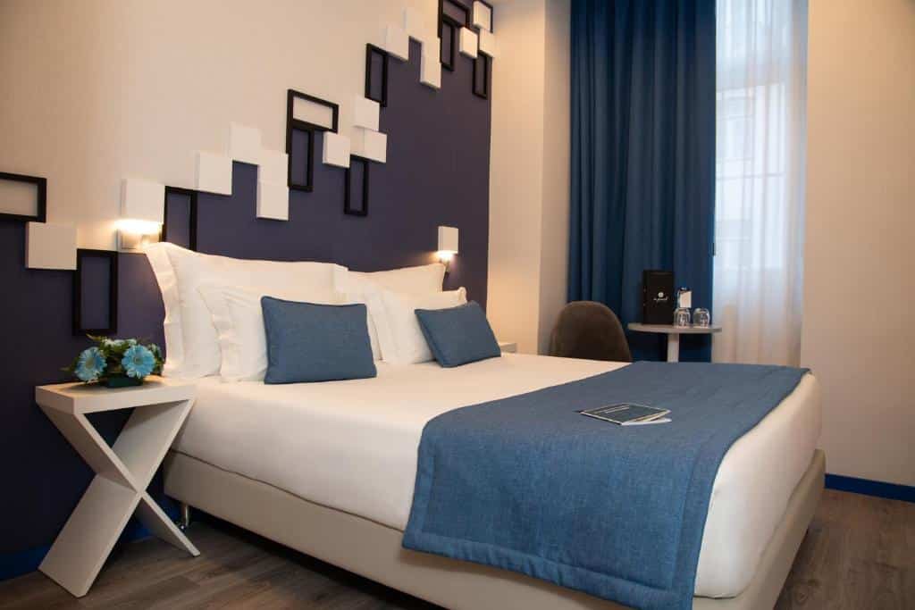 Quarto do Be Poet Baixa Hotel com uma cama de casal, janela com cortinas e uma pequena mesa com cadeira estofada.