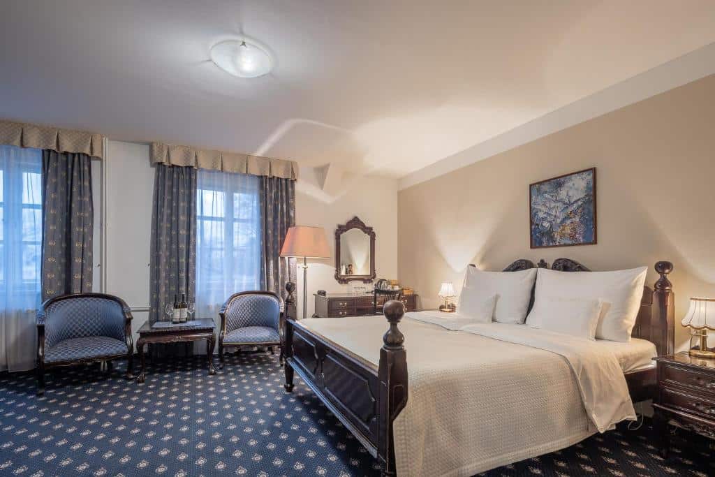 Quarto do Pytloun Old Armoury Hotel Prague, com cama de casal, duas cadeiras, secretária com espelho e candeeiros de cabeceira, de decoração clássica.