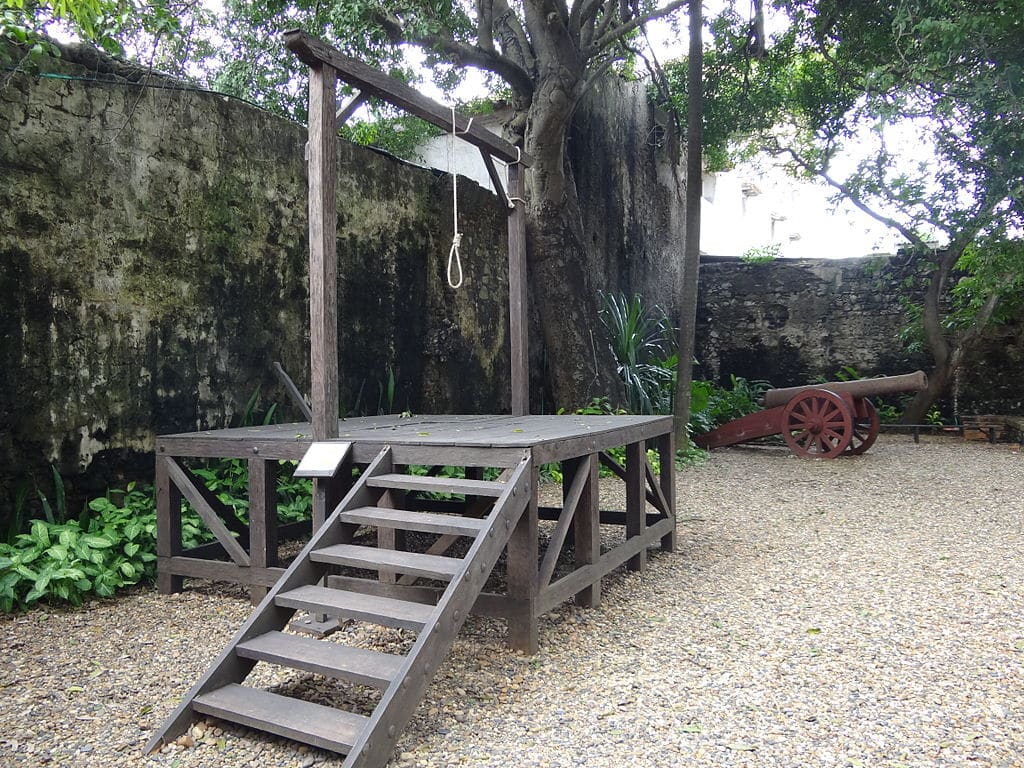Pátio de pedra do antigo Palácio da Inquisição, em Cartagena, com uma plataforma de madeira e um canhão antigo pintado de vermelho.