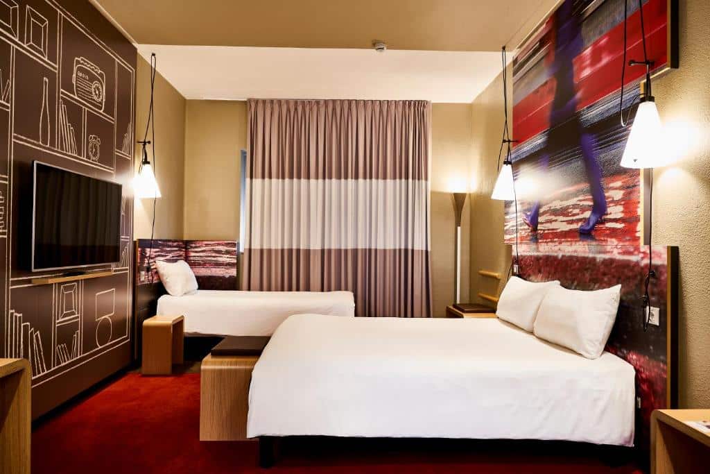 Quarto do Ibis Milano Centro com uma cama de casal, uma de solteiro, janela com cortinas, televisão e candeeiros suspensos do teto