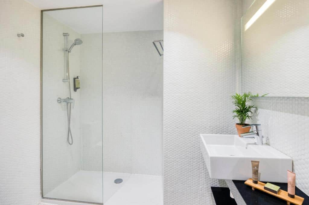 Casa de banho do Citadines Ramblas Barcelona, com cabine de duche, lavatório com produtos de higiene e um espelho na parede.