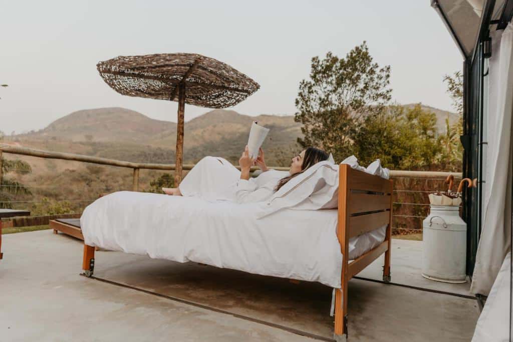 Mulher a ler um livro numa cama de dossel ao ar livre com vista para montanhas, perto da Rota do Vinho em São Roque