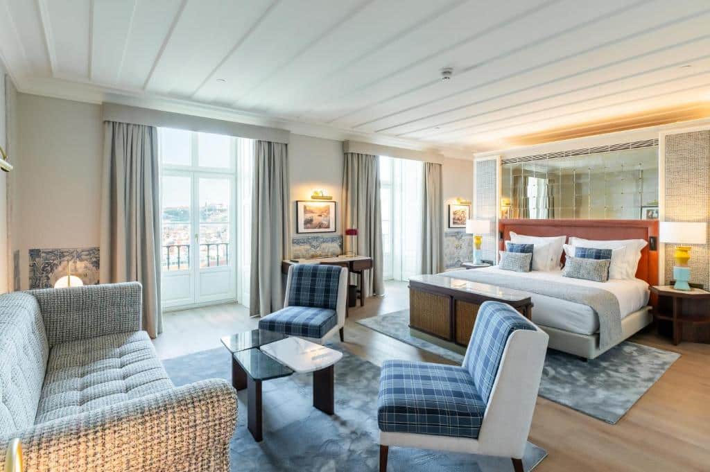 Quarto amplo do Palácio Ludovice Wine Experience Hotel, com cama de casal, duas varandas com cortinas, uma mesa de centro com duas poltronas estofadas, um sofá de dois lugares e dois tapetes