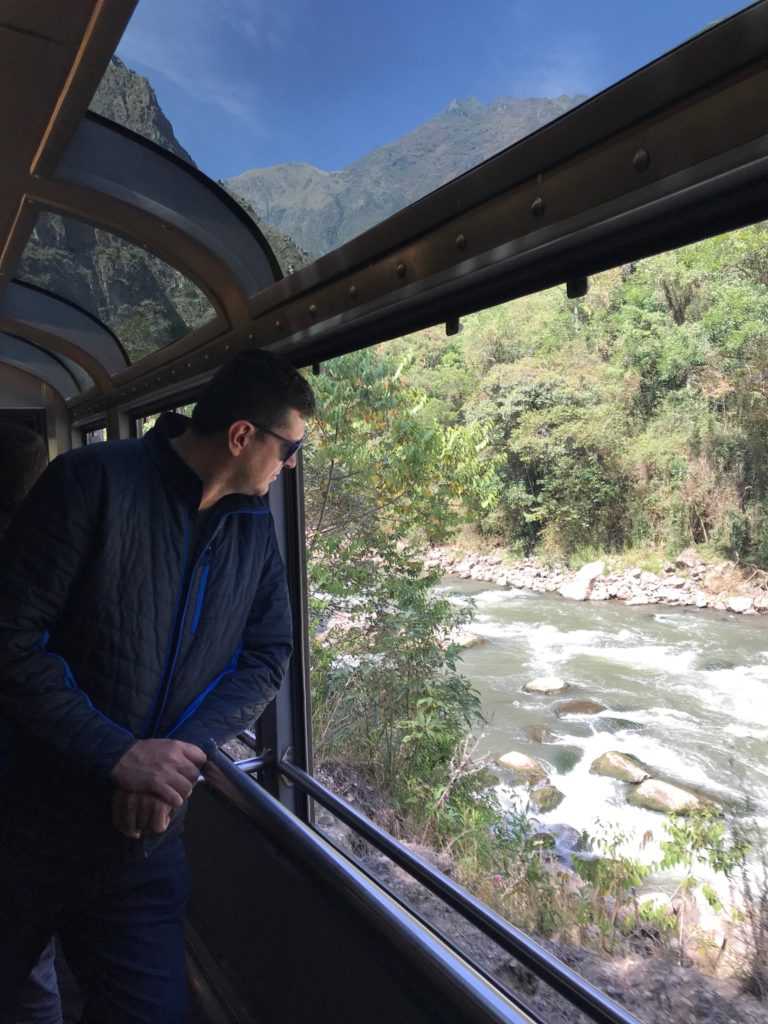 Passageiro no vagão panorâmico The 360 da Inca Rail, com vista para a paisagem entre Cusco e Machu Picchu
