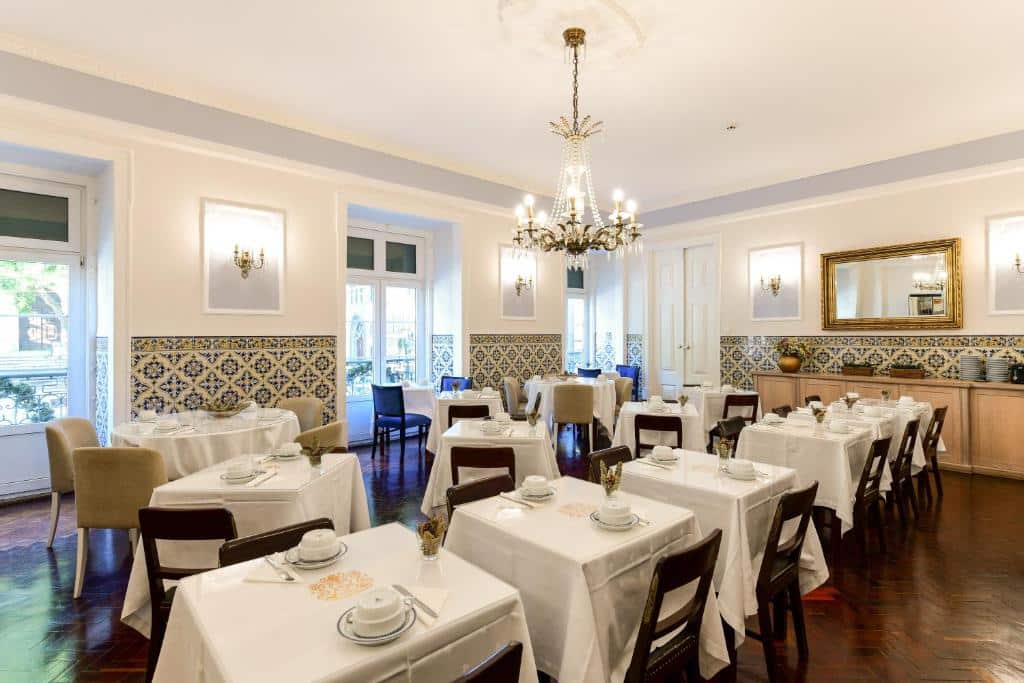 Sala de refeições do Casa de São Mamede Hotel com um lustre ao centro, várias janelas do lado esquerdo, mesas de madeira e azulejos nas paredes.