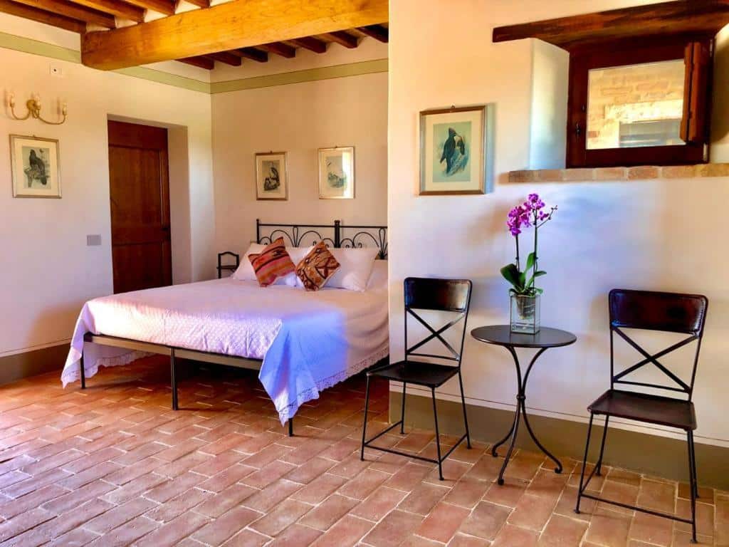 Quarto do Agriturismo Sole, com 23 m², chão de tacos, mesa pequena redonda preta com uma cadeira preta de cada lado, um quadro na parede em tons de azul e cama de casal com alguns quadros ao lado