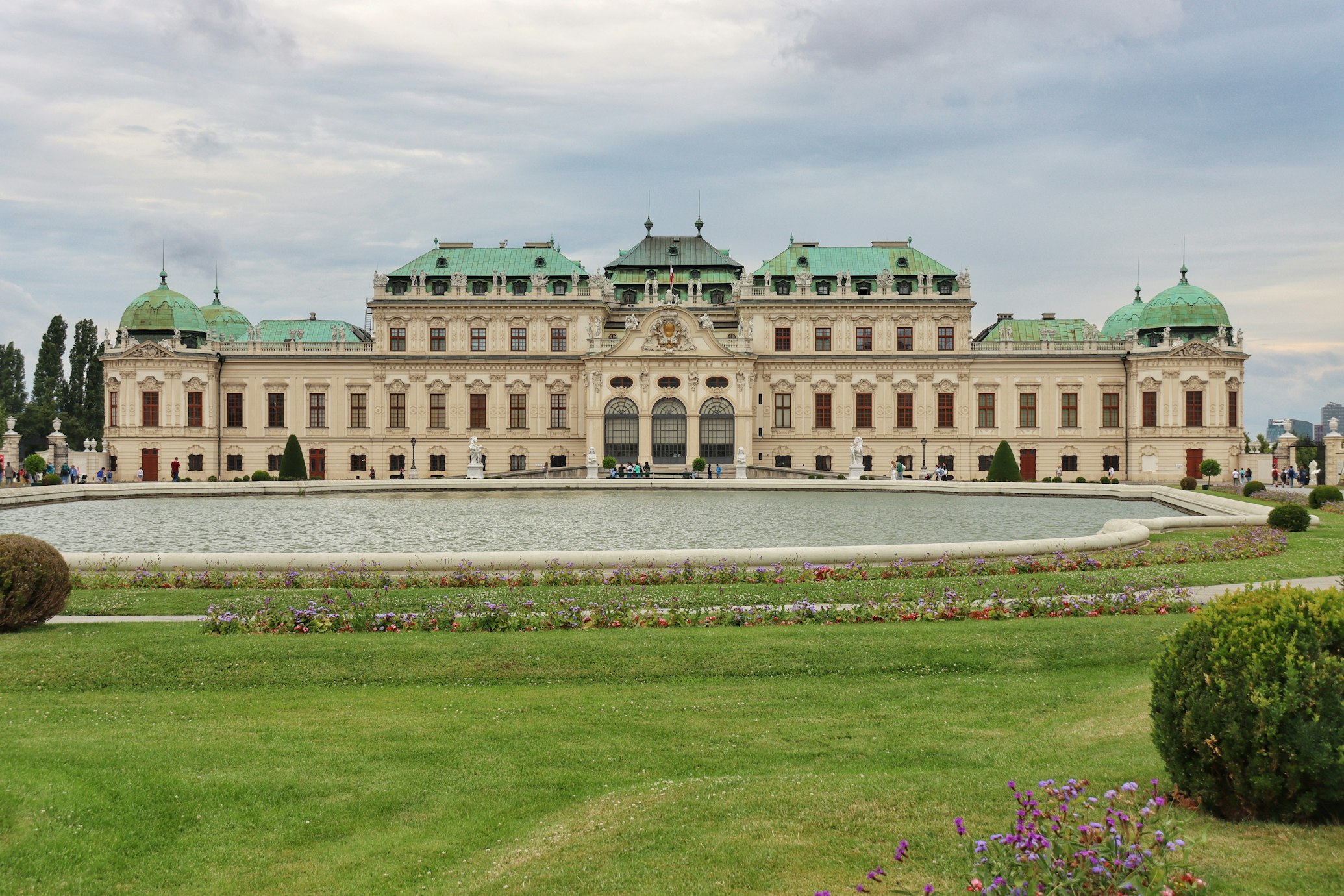 Palácio Belvedere com cúpulas verdes, grande pátio central e uma fonte decorativa em primeiro plano, sob céu nublado.