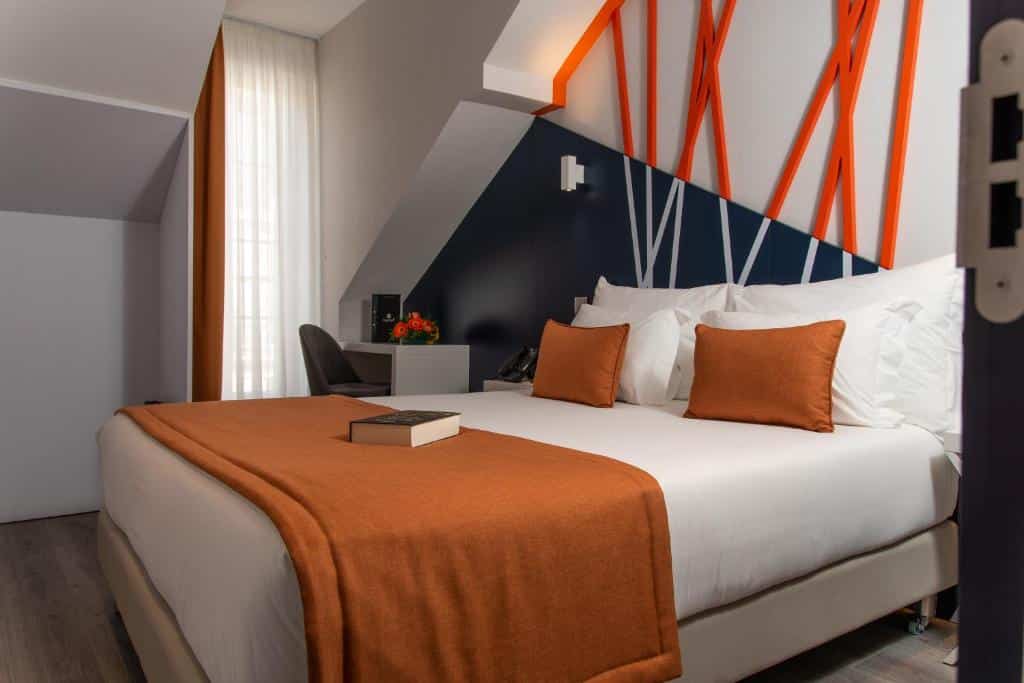 Quarto do Be Poet Baixa Hotel com cama de casal, uma janela com cortina do lado esquerdo e, junto dela, uma secretária com cadeira