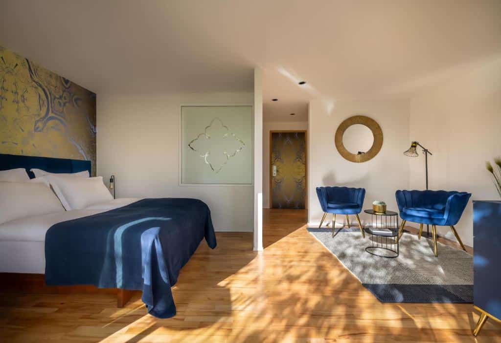 Quarto de hotel moderno com cama de casal azul, decoração em tons dourados e poltronas azuis, no Falkensteiner Hotel Adriana l Adults Only, em Borik
