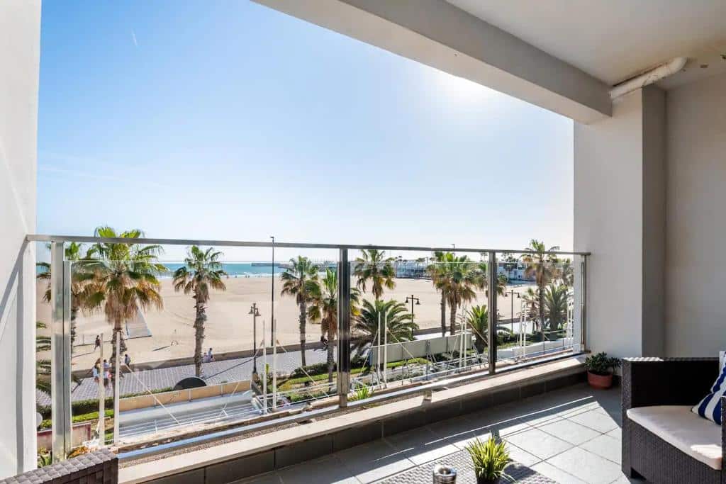 Edifício de apartamentos soalheiro com vista para uma praia com palmeiras e pessoas a caminhar pela orla, junto ao Moderno apartamento con vistas al mar.