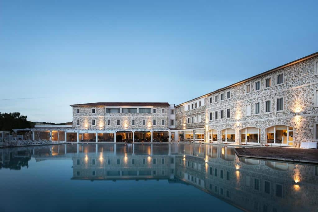 Piscina grande de um dos hotéis na Toscana, o Terme di Saturnia Natural Spa &amp; Golf Resort, a espelhar os edifícios de tijolo à vista