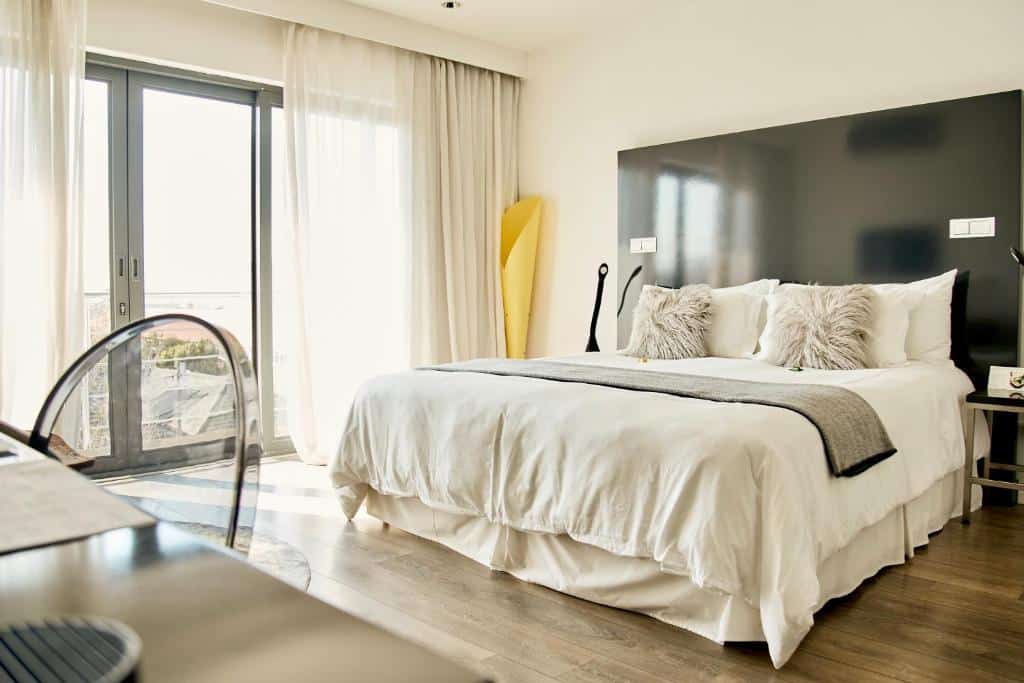 Quarto no DysArt Boutique Hotel com cama grande, almofadas macias, cabeceira cinzenta e cortinas transparentes.
