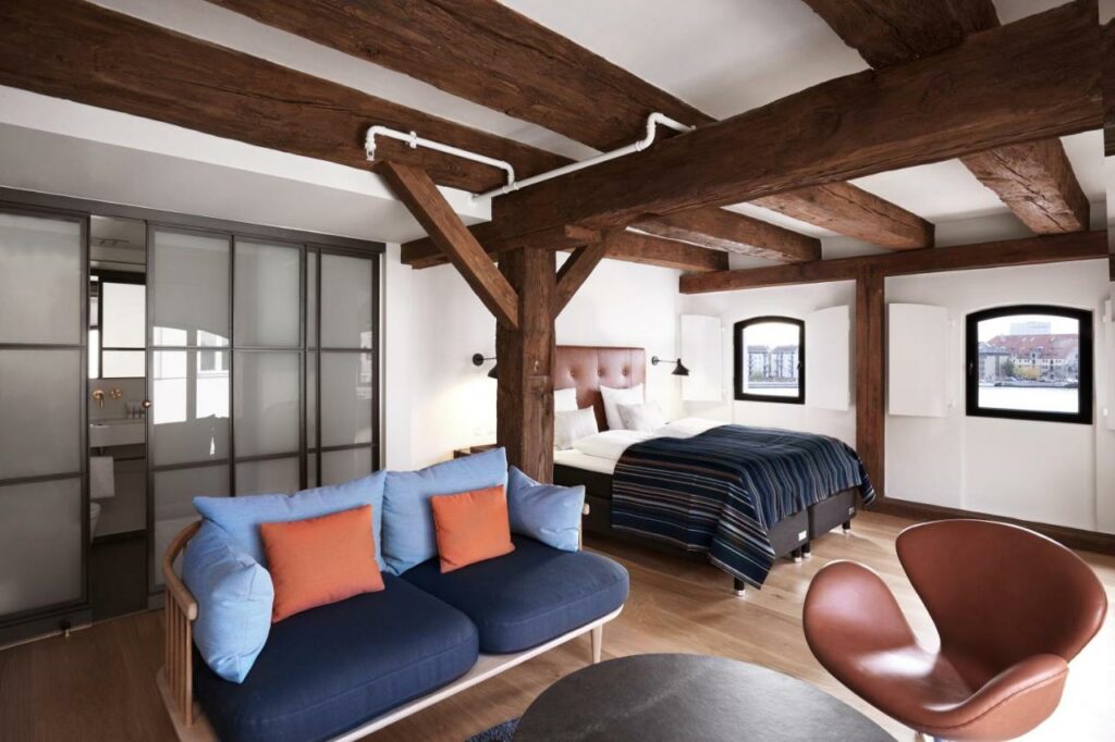 Quarto do 71 Nyhavn Hotel com duas camas a formar uma cama de casal, um sofá, mesa, cadeira e duas janelas.