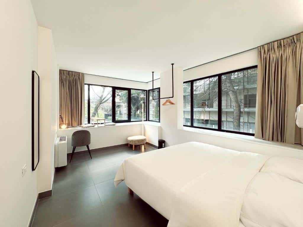 Quarto com amplas janelas com vista para árvores e mobiliário moderno e minimalista, incluindo cama, cadeira e prateleira