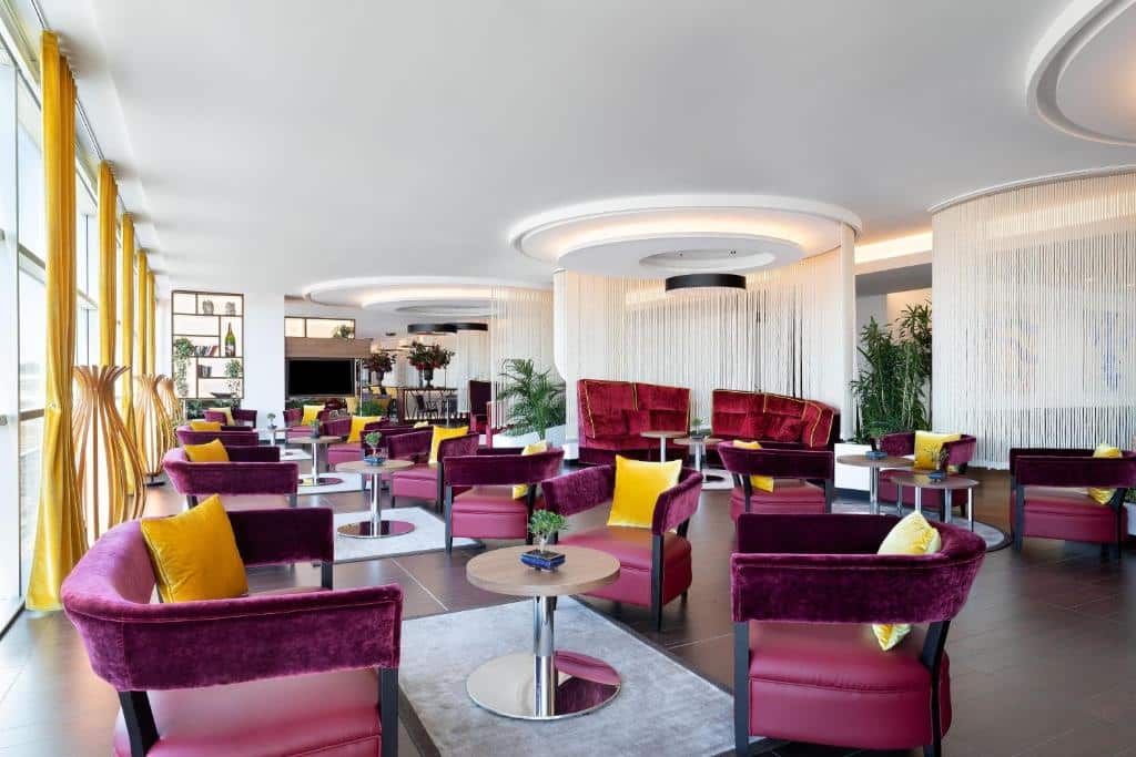 Zona de convívio do Sheraton Milan Malpensa Airport com várias poltronas estofadas em tom bordô e almofadas douradas, num ambiente requintado
