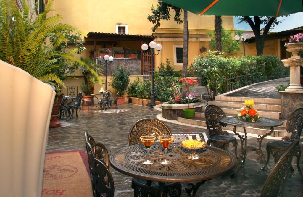 área comum do Hotel Villa San Lorenzo Maria, um dos hotéis baratos em Roma, com mesa e cadeiras de ferro vintage, um pátio grande com coretos e plantas verdes em redor
