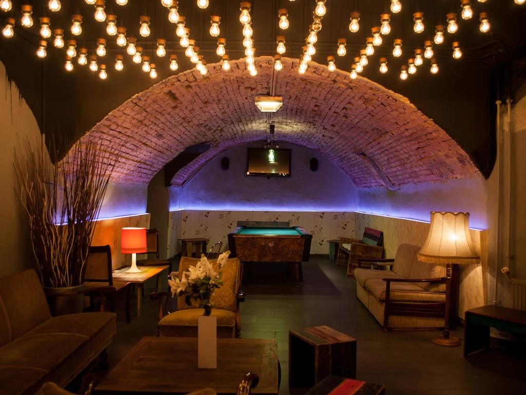 Sala de estar abobadada em tijolo no Wombat's City Hostel, com sofás, uma mesa de bilhar e candeeiros suspensos.