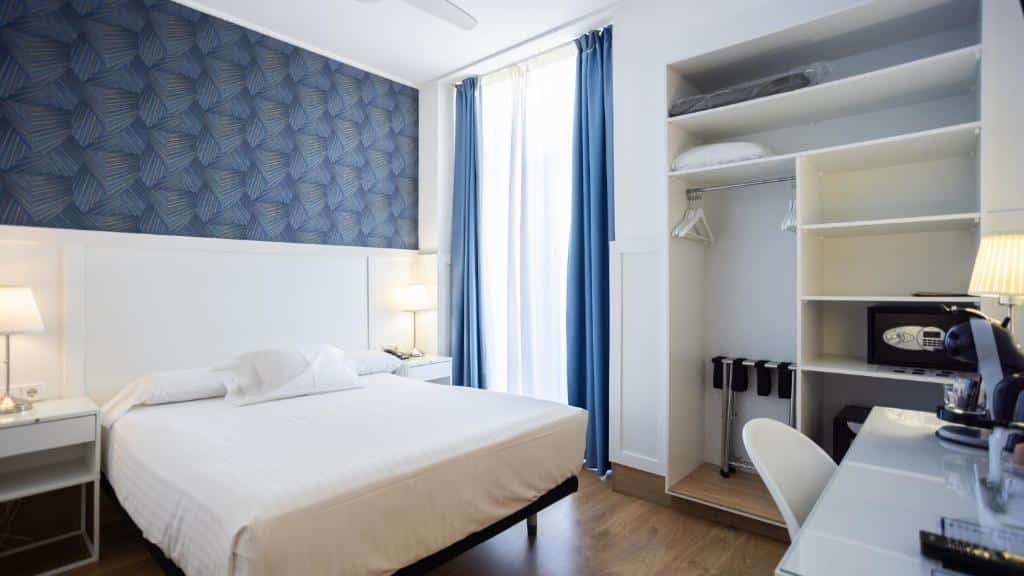 Quarto do Venecia Plaza Centro com parede decorada em tons de azul, cama de casal com roupa de cama branca, roupeiro embutido com cabides e prateleiras e uma pequena mesa com máquina de café.